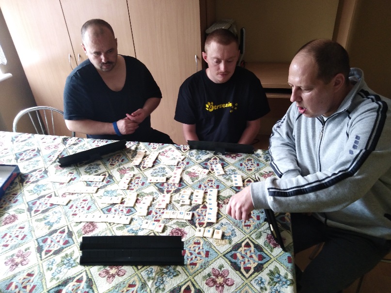 Trzech mężczyzn  przy stolę grających w grę stolikową. 