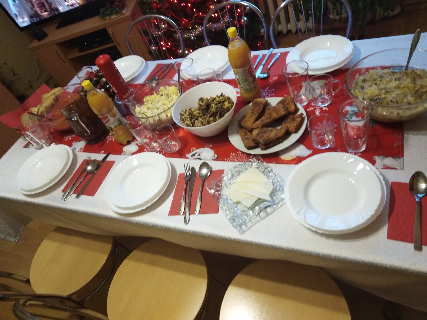 Stół z nakryciami wigilijnymi i wieloma potrawami.