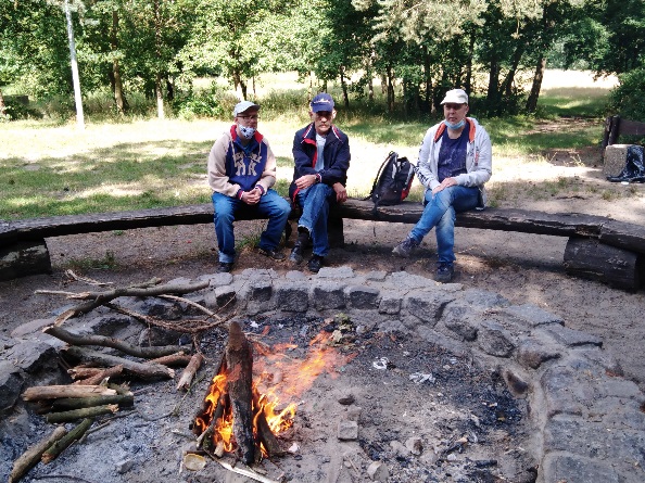  Trzech mężczyzn na tle lasu  przed nimi  palące się ognisko. 