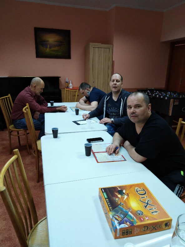 Grupa mężczyzn siedzących przy stole oraz grę DIXIT.