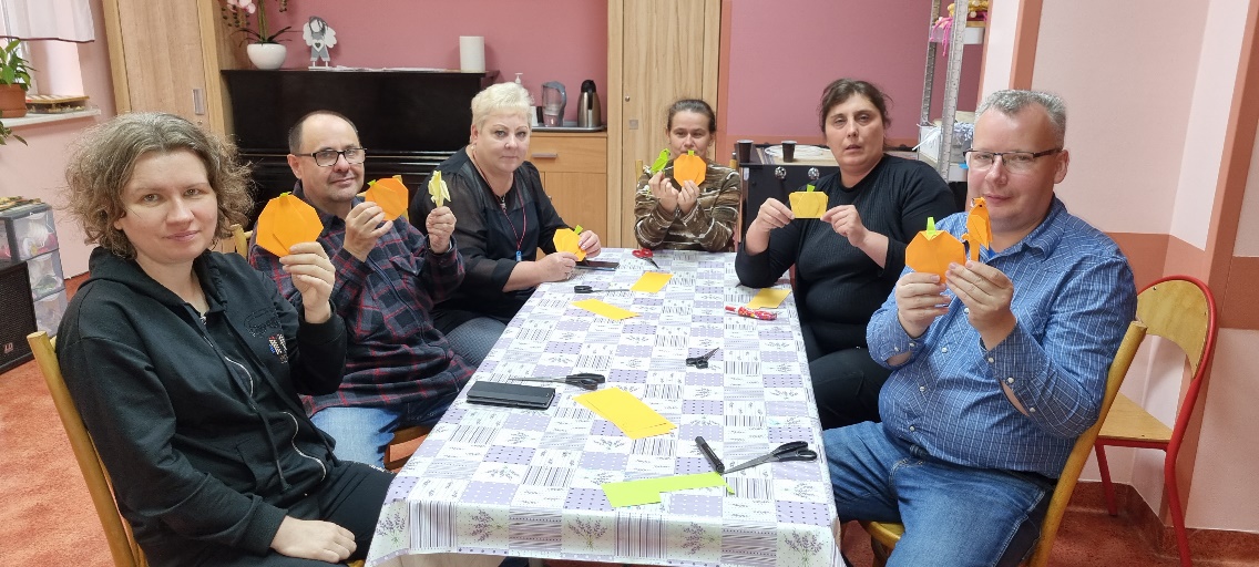 Grupa osób siedzących przy stole pokazuje wykonane przez siebie origami.