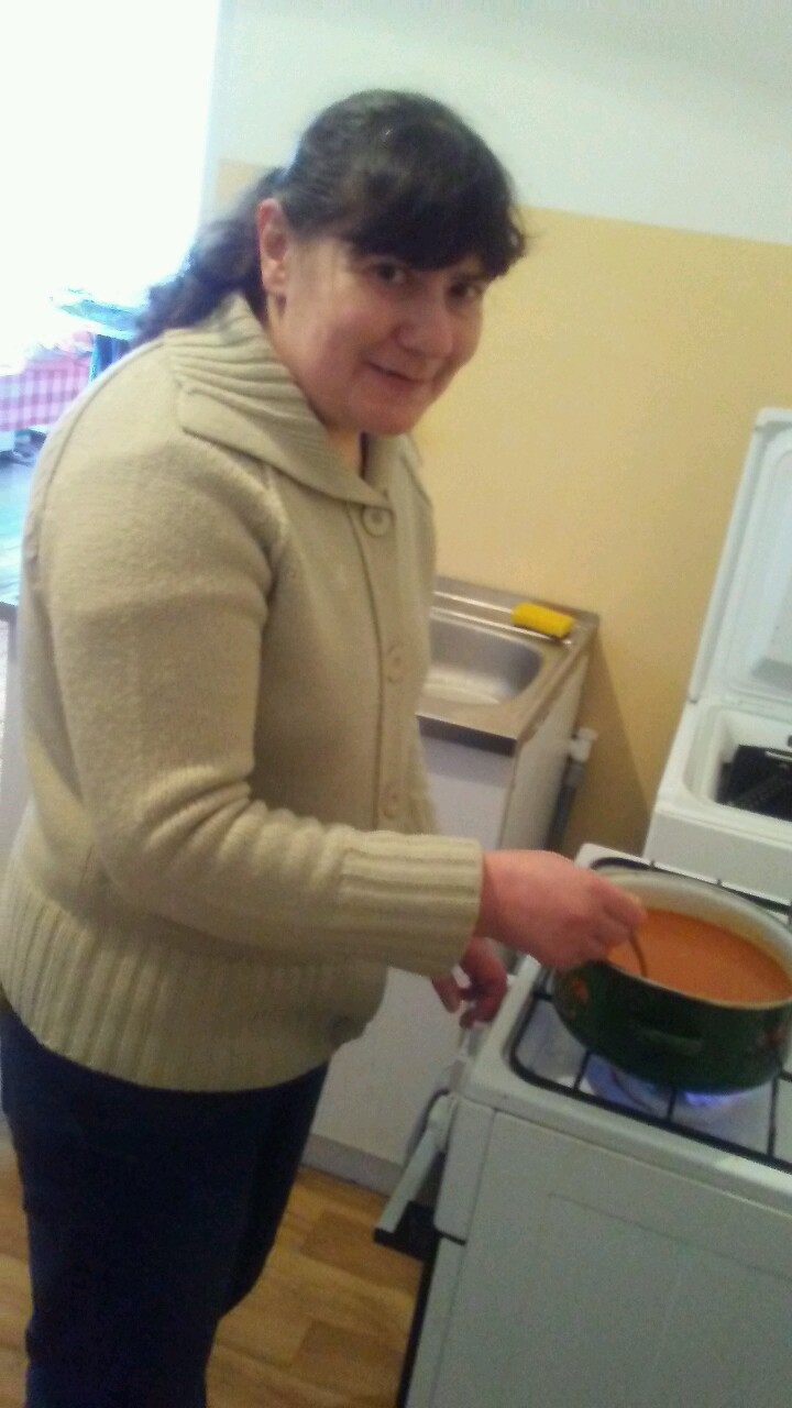 Kobieta podgrzewająca zupę pomidorową na kuchence gazowej. 
