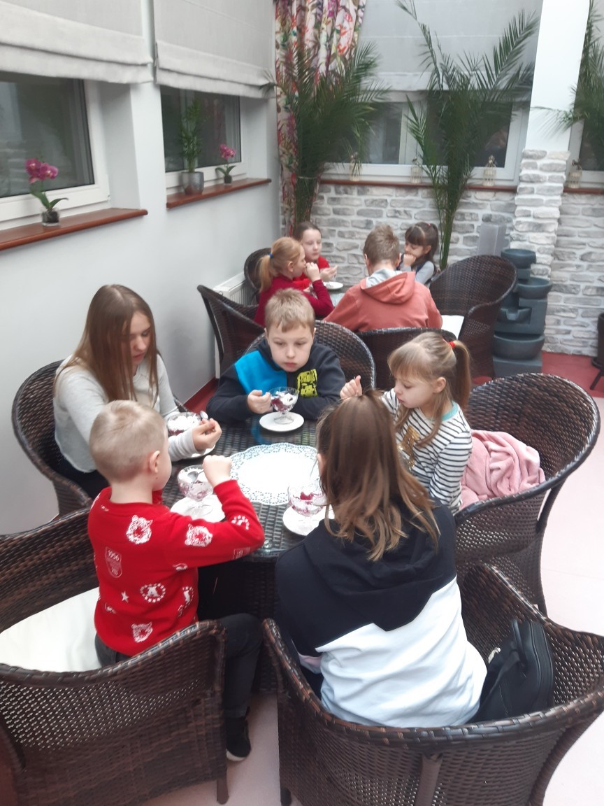 Grupa dzieci siedząca przy stolikach w kawiarni, delektująca się deserami. 