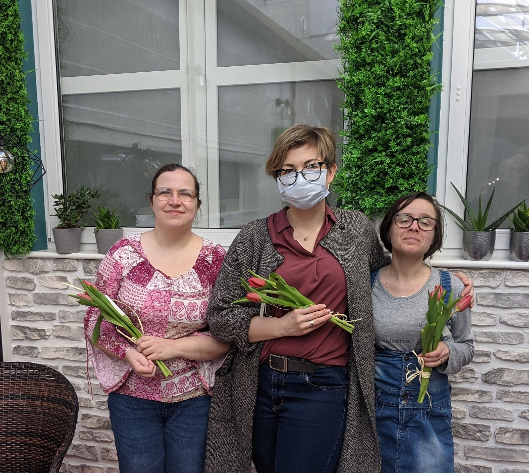 Trzy kobiety stoją z tulipanami pod ścianą.