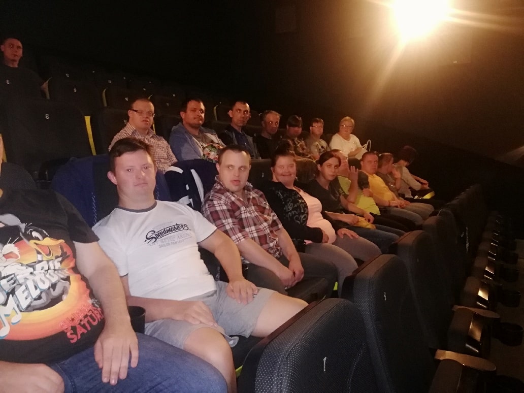W sali kinowej uczestnicy siedzą w fotelach zajmując dwa rzędy. 