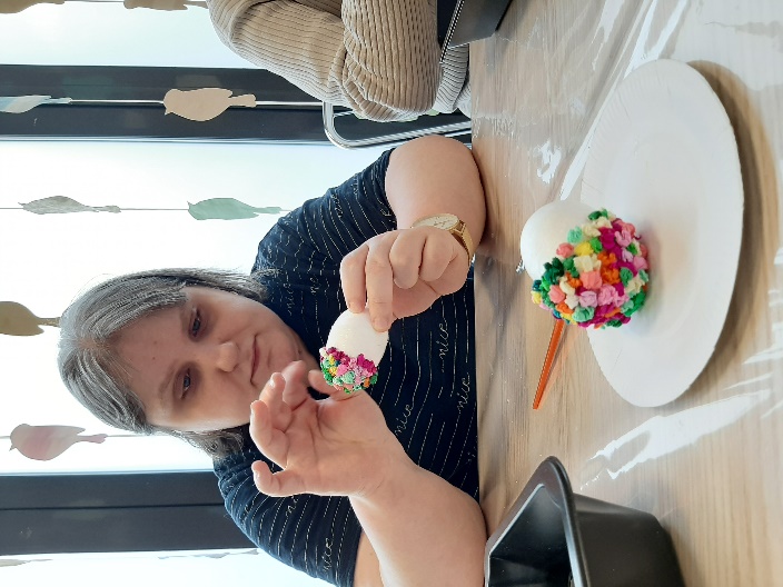 Kobieta przyklejająca kolorowe kulki z bibuły do styropianowego jajka.
