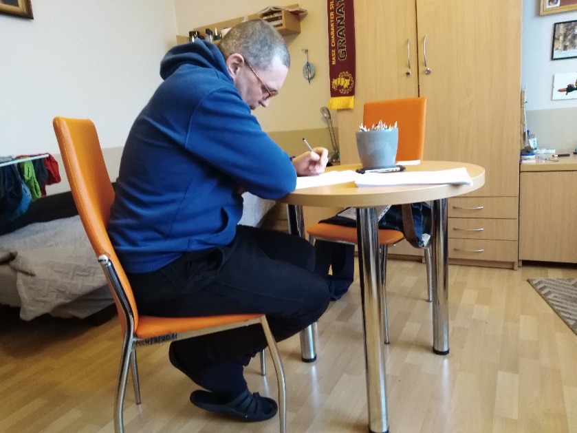 Mężczyzna siedzący przy stoliku,  rozwiązujący ćwiczenia.