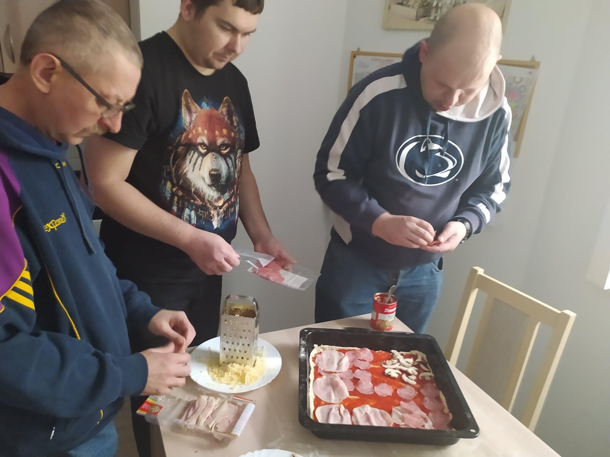 Trzech mężczyzn przygotowuje pizzę.