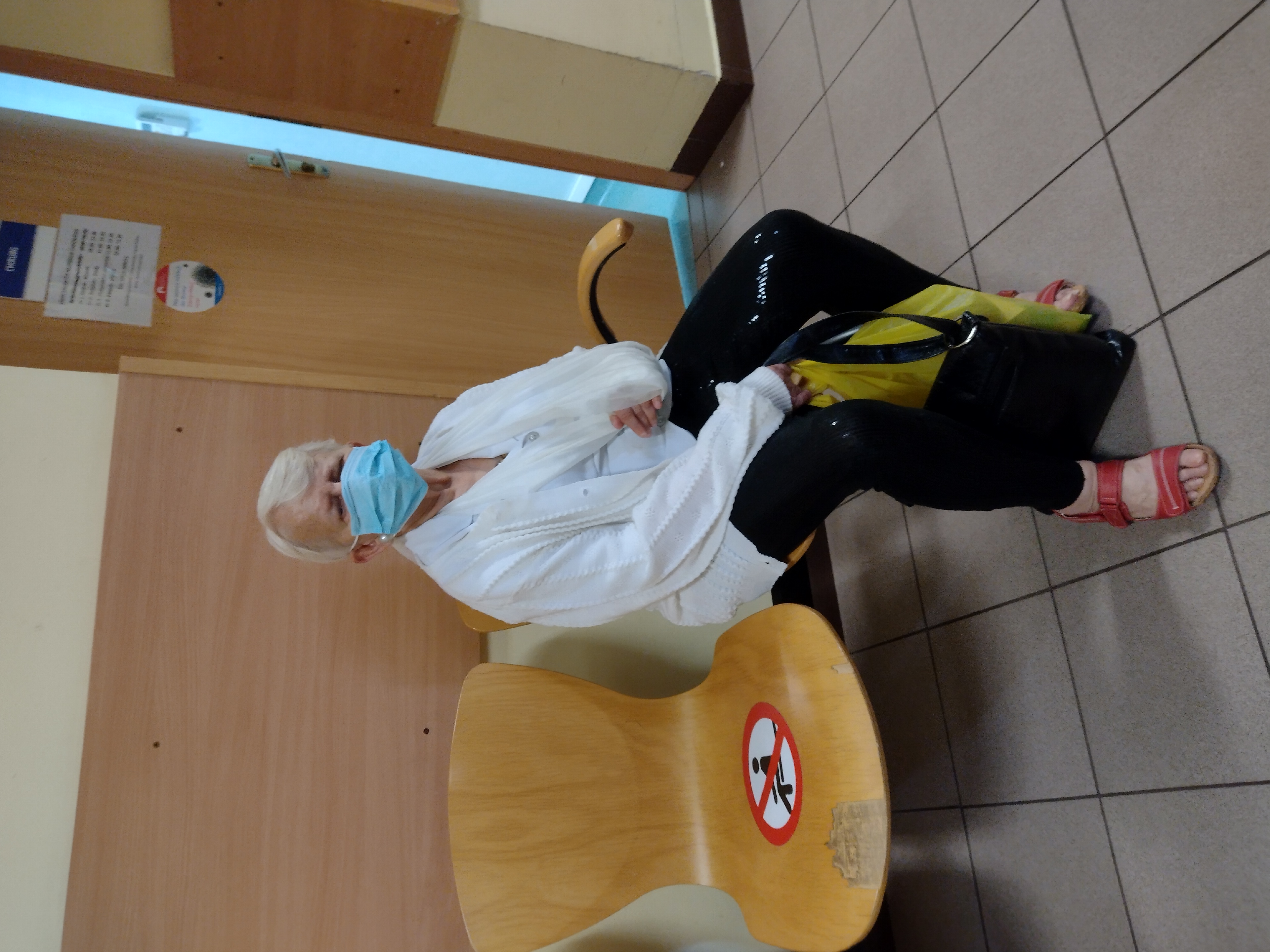 Kobieta z ręką w gipsie siedzi przed gabinetem lekarskim