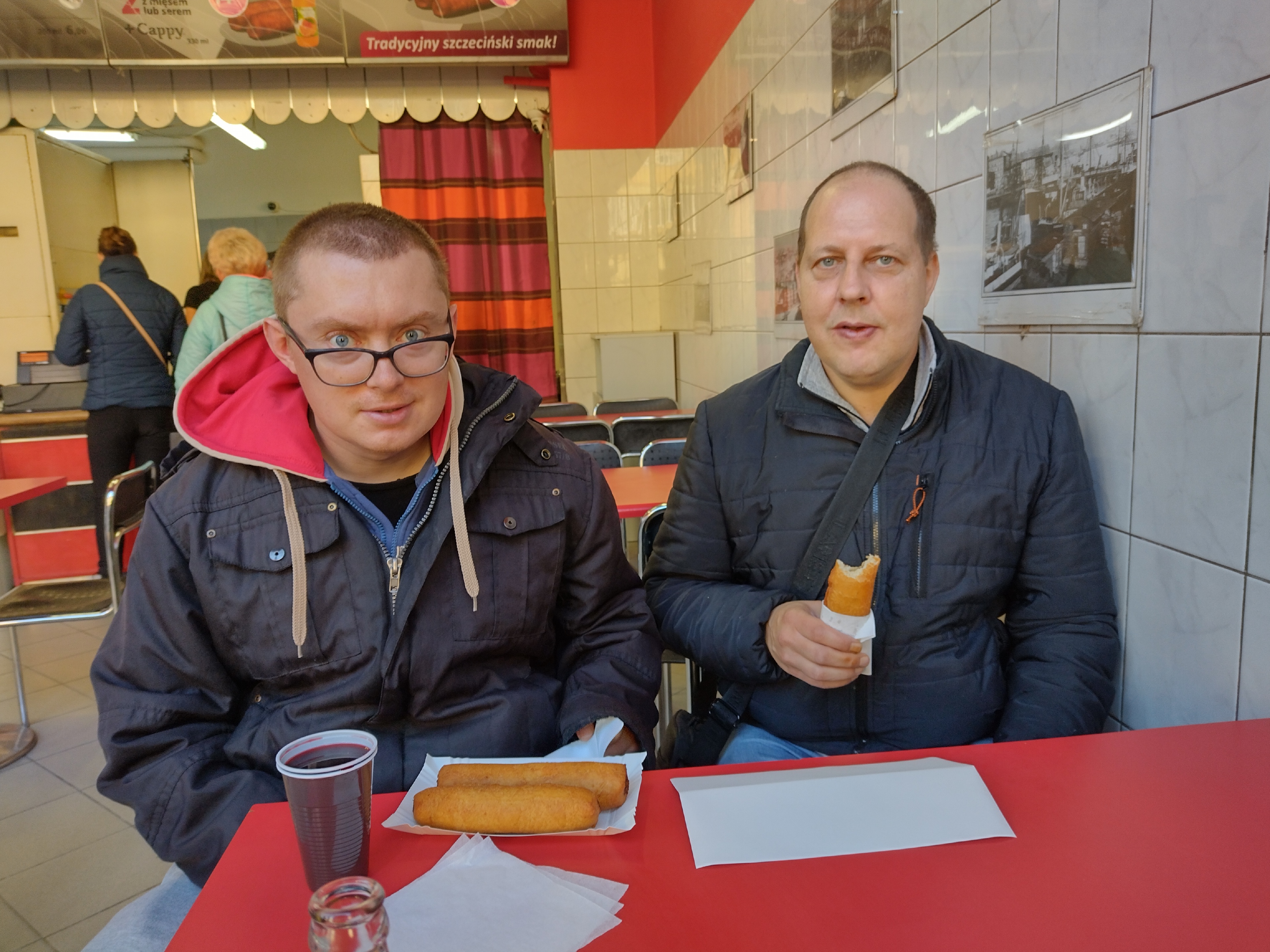 Dwóch mężczyzn w barze jedzą paszteciki szczecińskie. 
