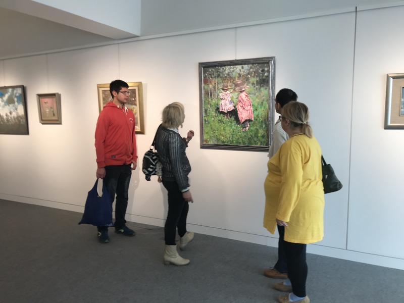 Dwie kobiety i dwóch mężczyzn oglądają wystawę obrazów malarskich.