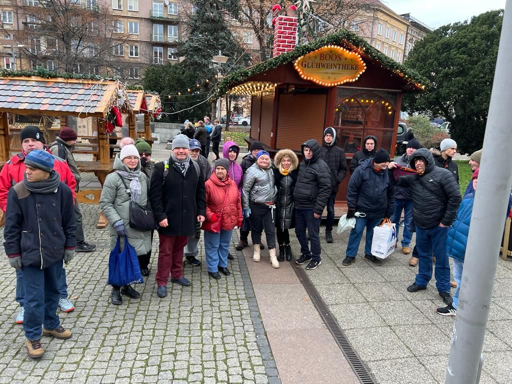 Grupa kobiet i mężczyzn pozuje do zdjęcia  na tle  stoiska Bożonarodzeniowego.    