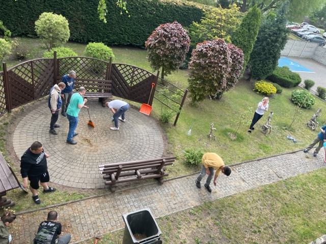 Grupa mężczyzn i kobieta sprzątają  w ogrodzie.  
