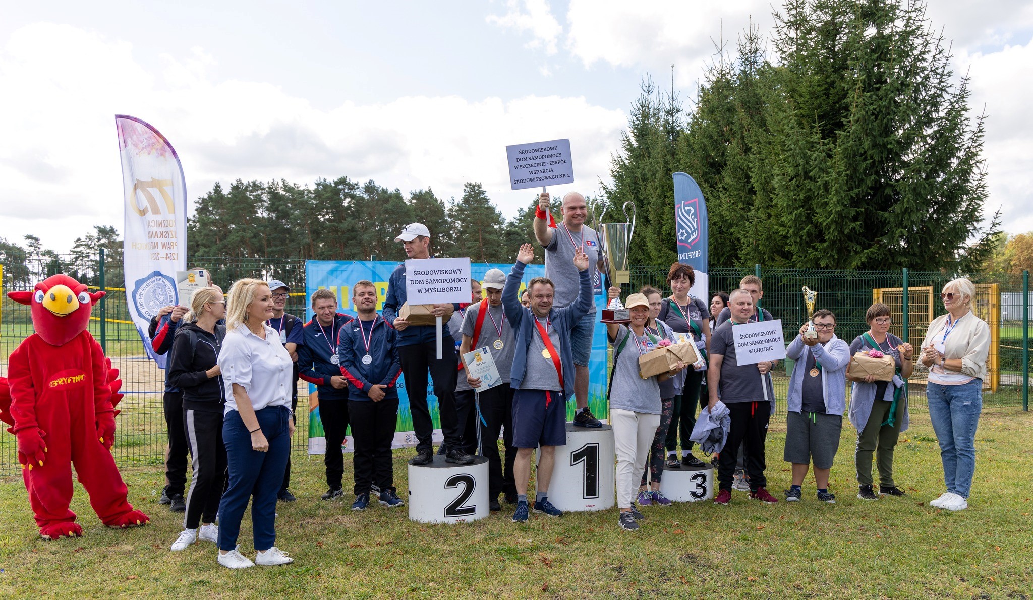 Grupa wielu radosnych osób zajmuje miejsca na podium. 