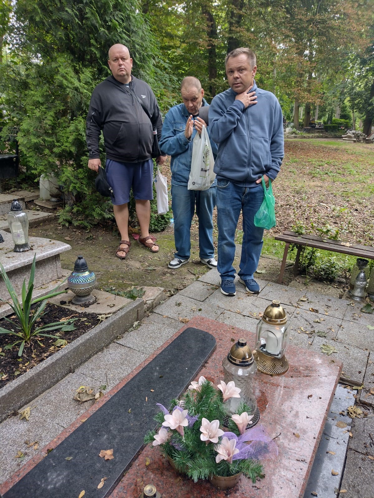 trzech mężczyzn stoi na cmentarzu przed grobem. 