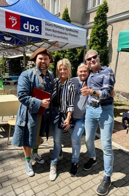 Dwie kobiety i dwóch mężczyzn w słoneczny dzień pozują do zdjęcia. Mężczyzna po lewej jest przebrany w strój pirata. 