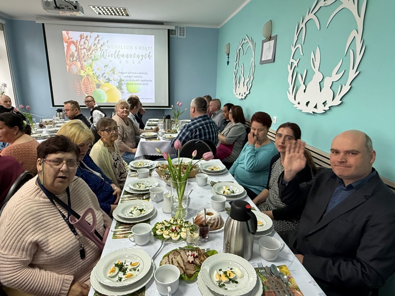 Gruba kobiet i mężczyzn pozuje do zdjęcia. Na stole potrawy wielkanocne, oraz sztućce i naczynia. 