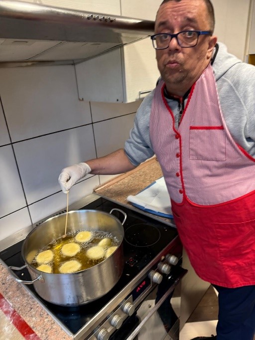 Mężczyzna stoi przy kuchence i smaży pączki.