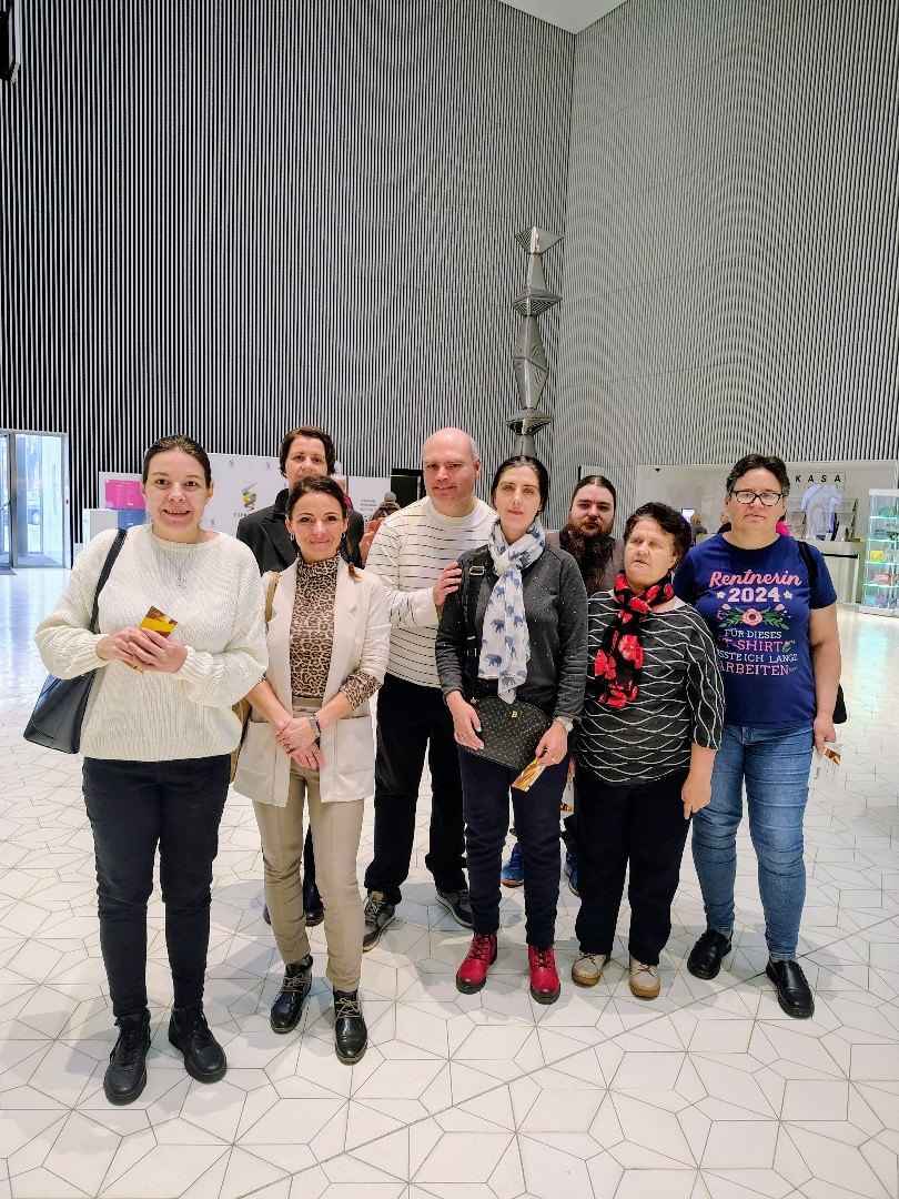 Grupa osób stoi w nowoczesnym holu Filharmonii Szczecińskiej z jasną podłogą i wysokimi ścianami w pionowe linie.