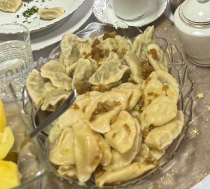 Szklany półmisek pełen pierogów polanych skwarkami z cebuli, ustawiony na elegancko nakrytym stole.