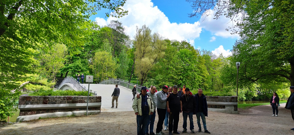 Grupa osób w parku stoi przed mostem.
