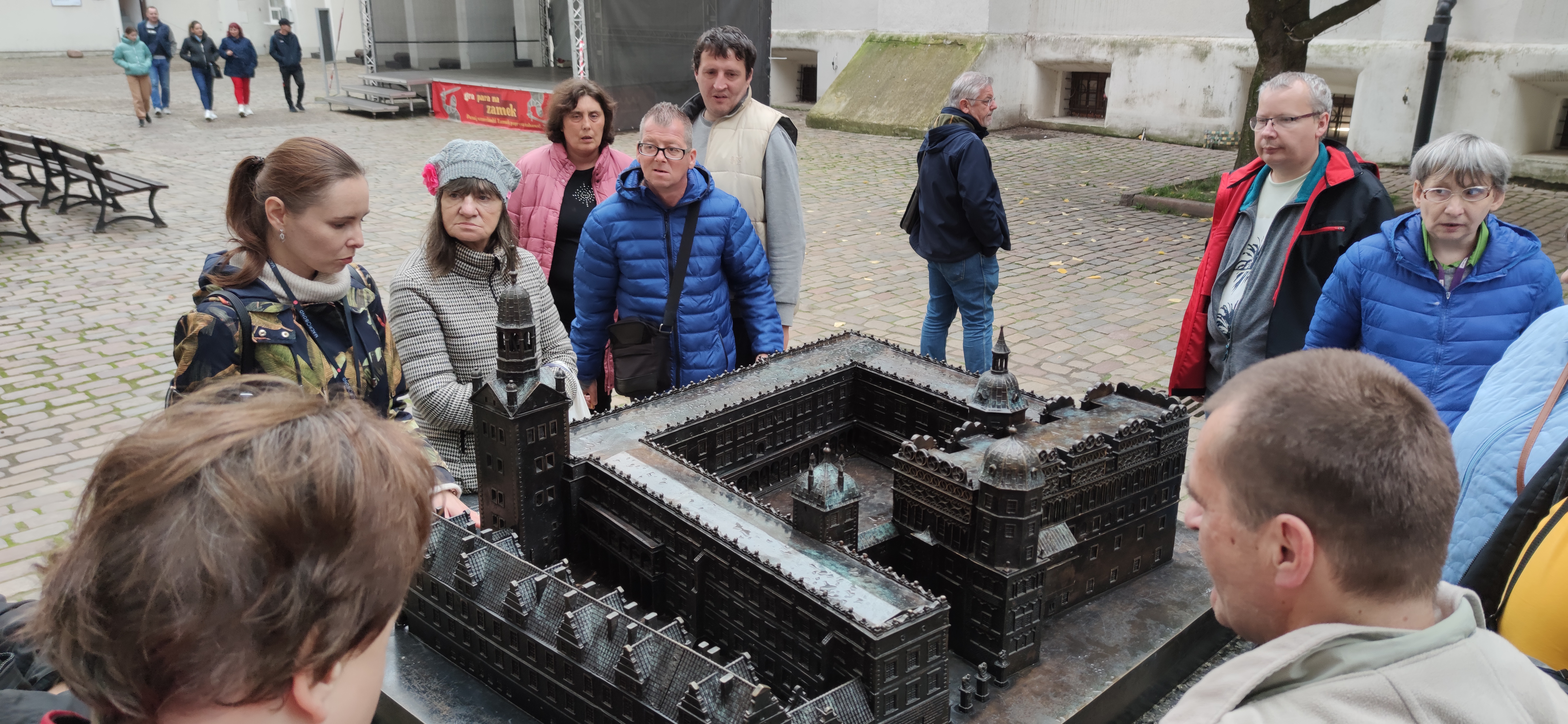 Grupa osób stoi przy żelaznej makiecie zamku.