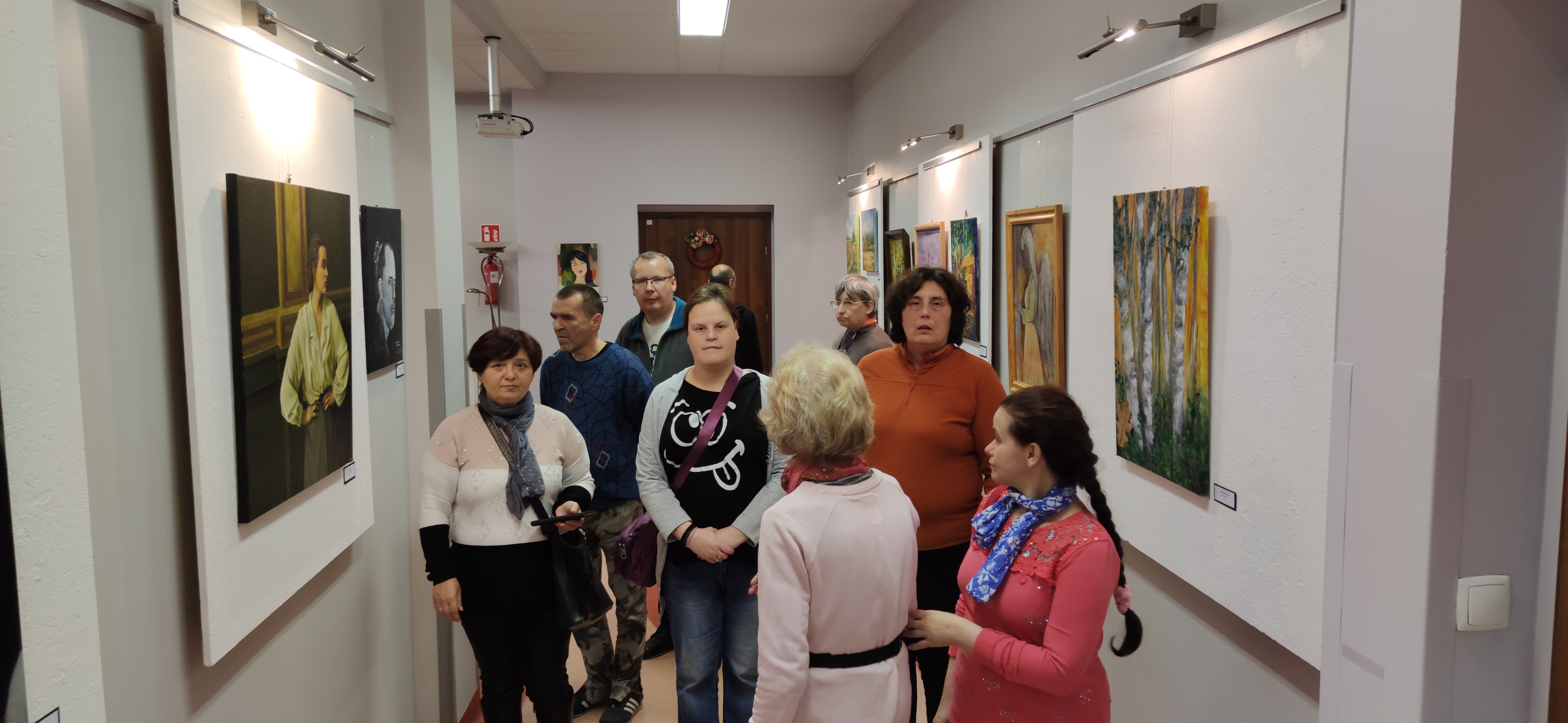 Grupa osób ogląda obrazy w galerii na ścianach.