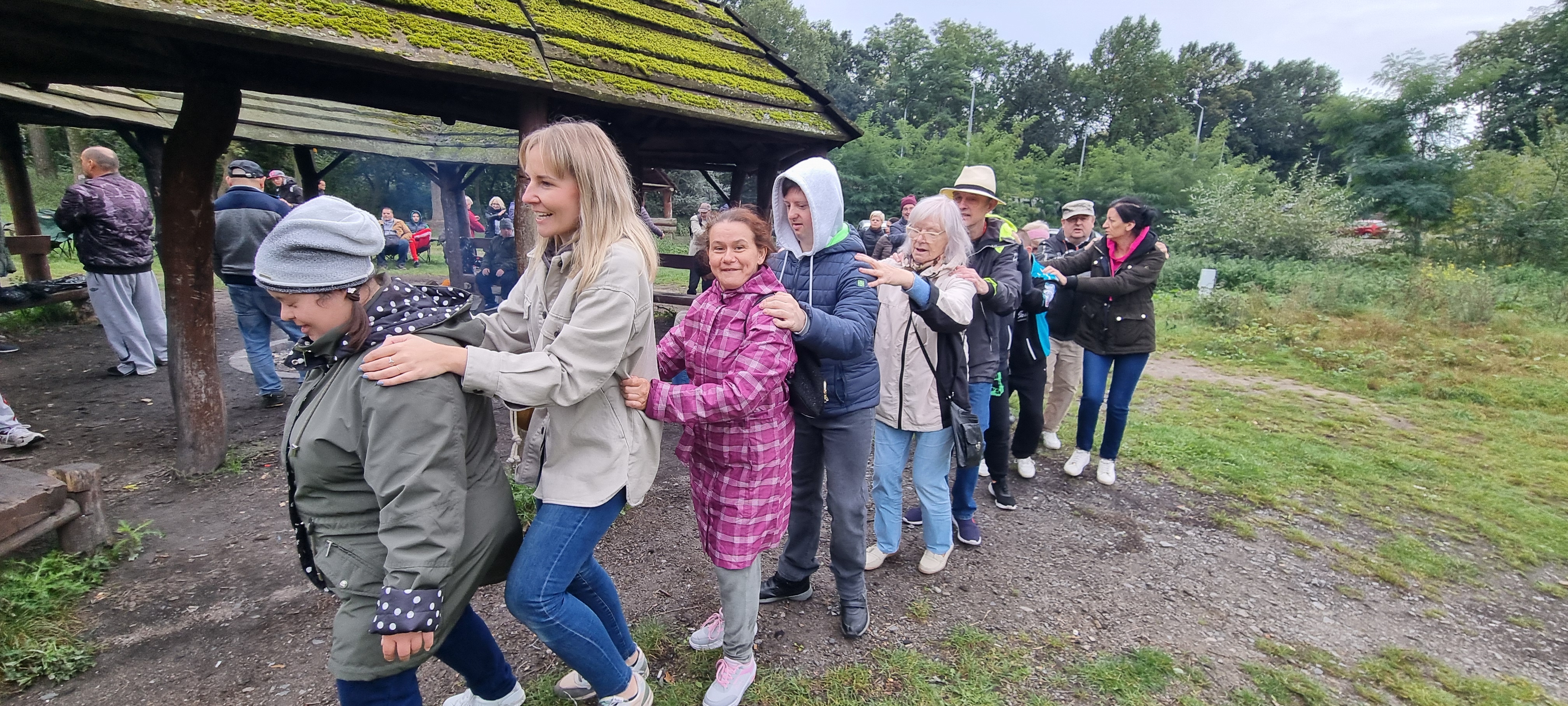 Grupa osób idzie jeden za drufim tanecznym krokiem.