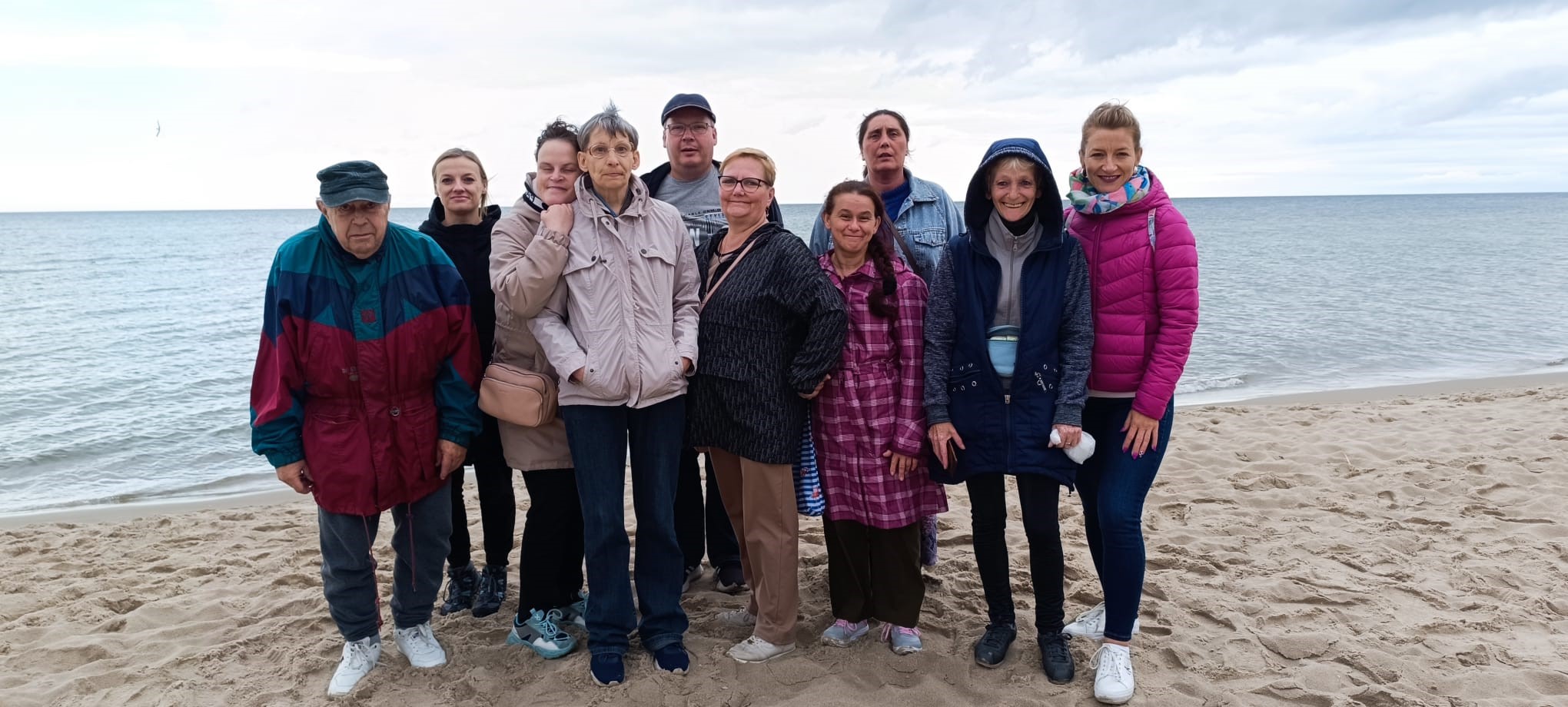 Grupa osób pozuje do zdjęcia na plaży na tle morza.