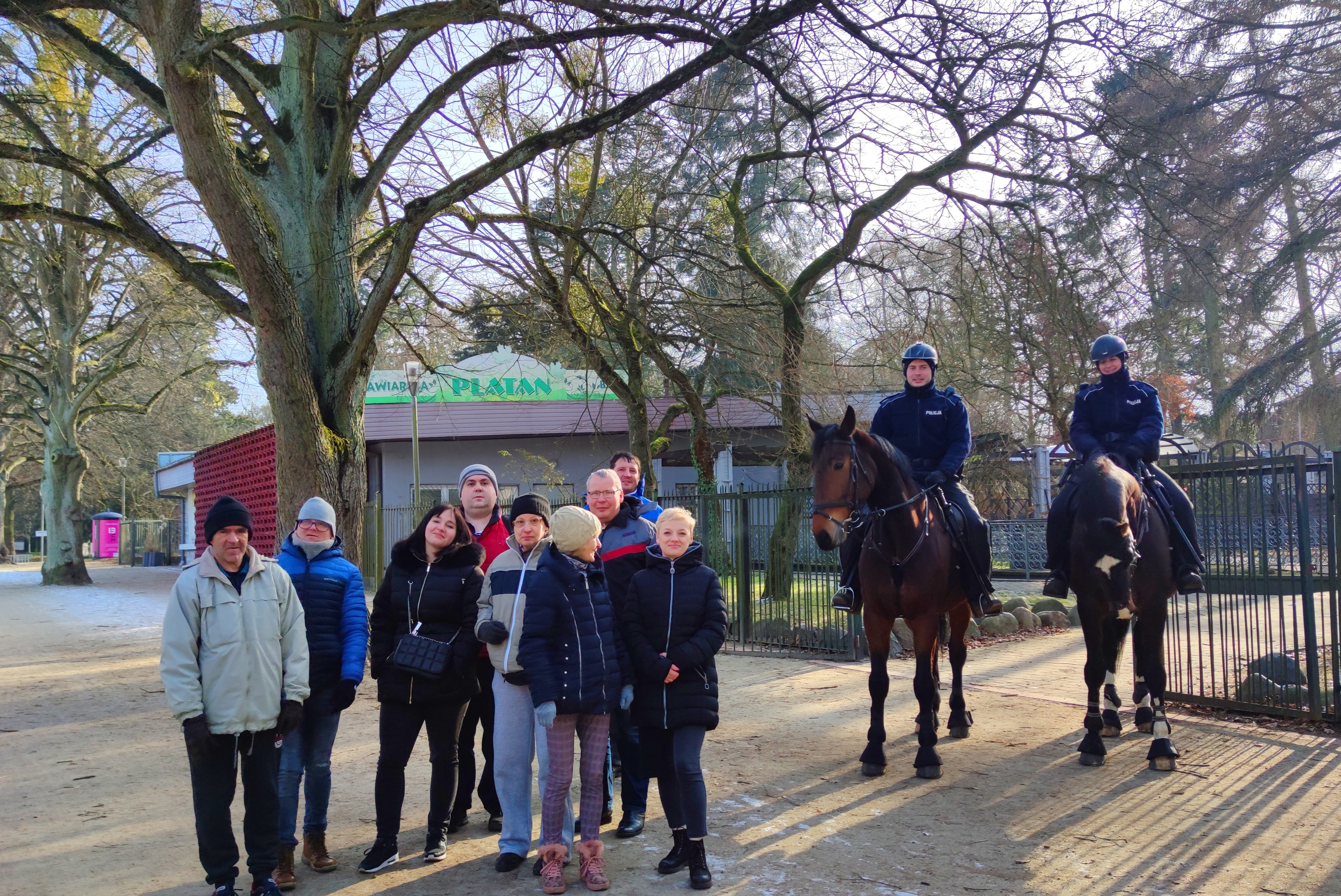 Grupa osób w parku i policjanci na koniach.