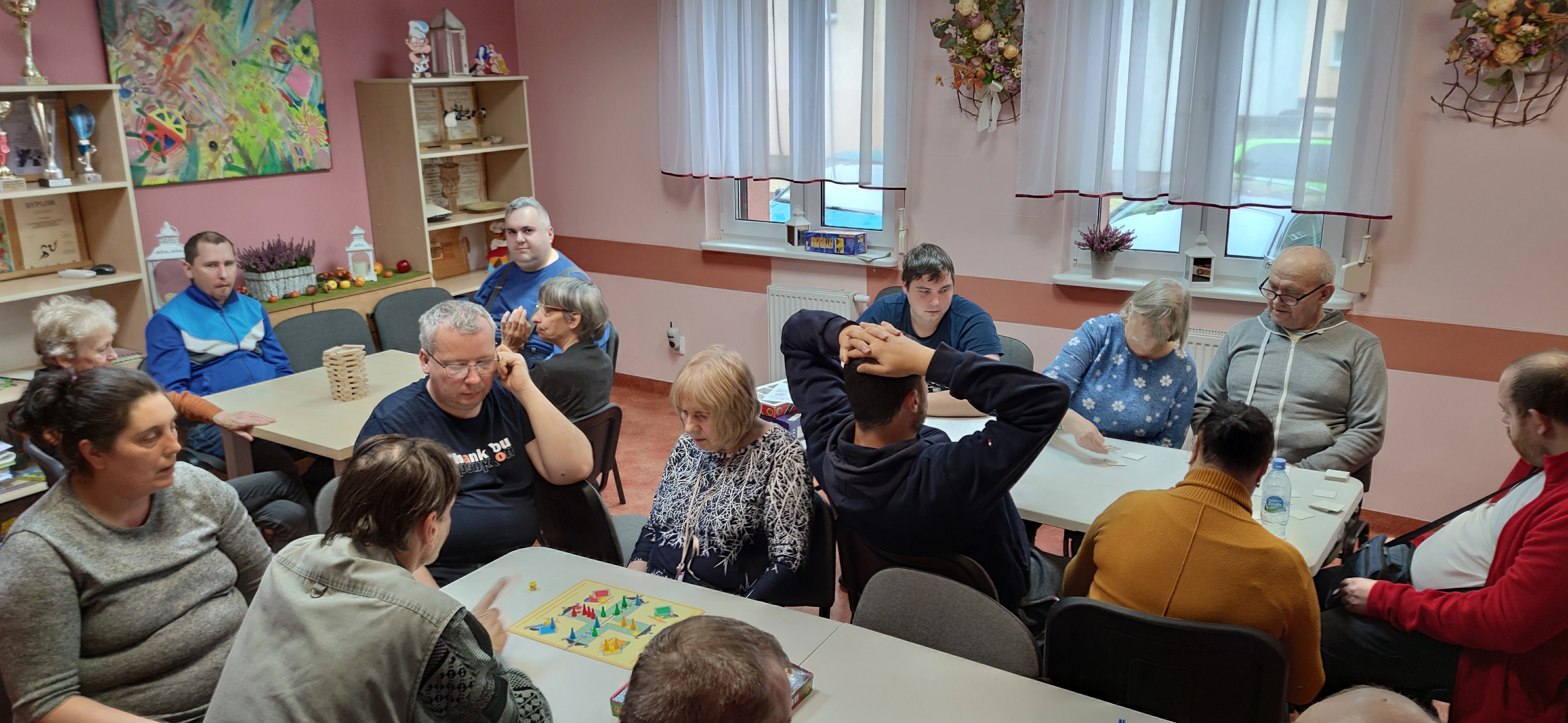 Grupa osób przy stołach gra w różne gry.