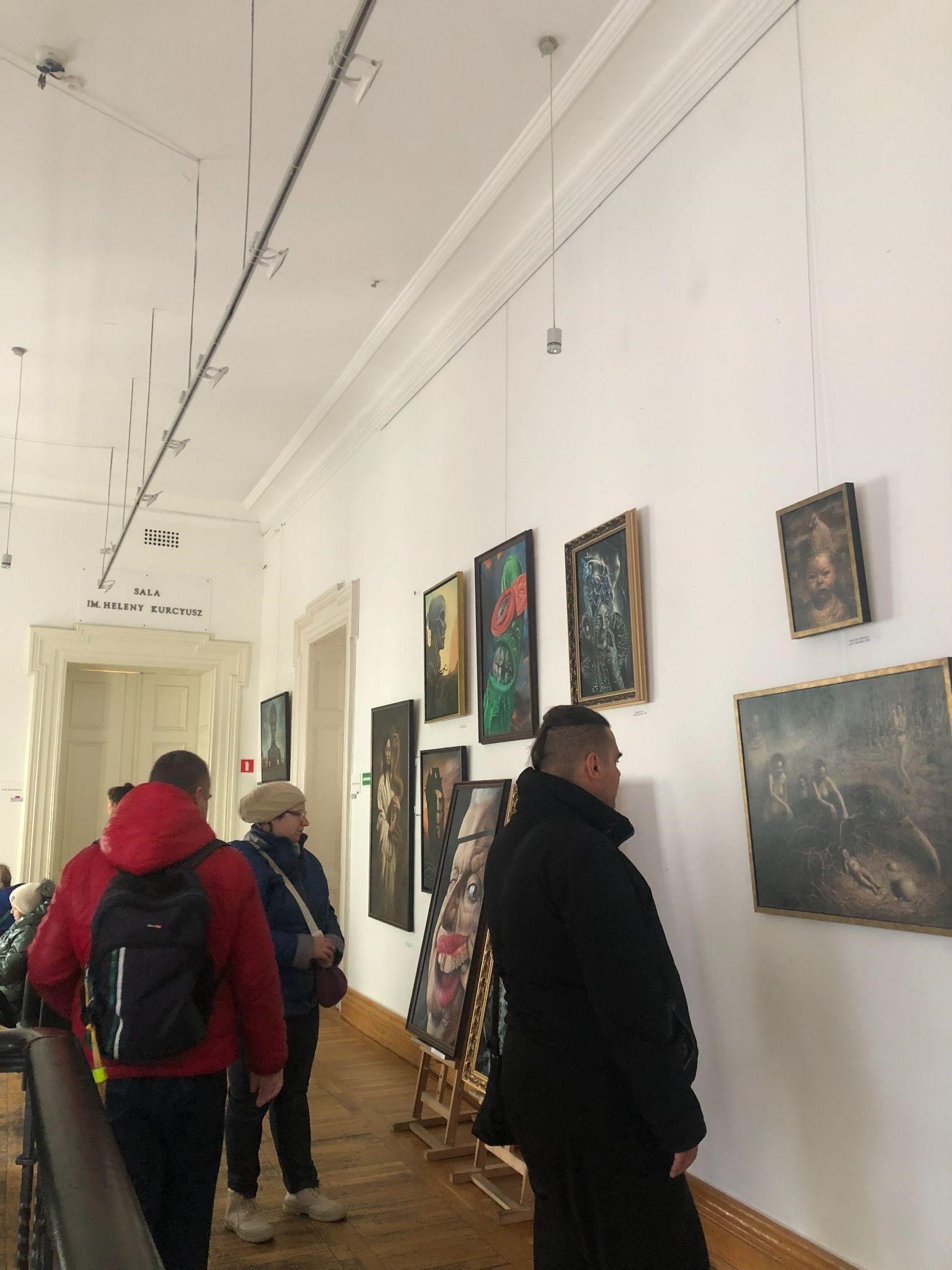 Ludzie oglądający prace malarskie na wystawie. 