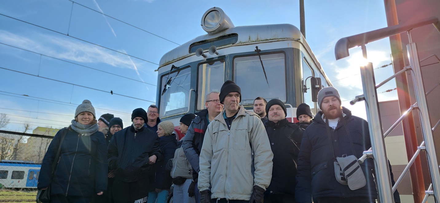 Grupa osób stoi przed lokomotywą.