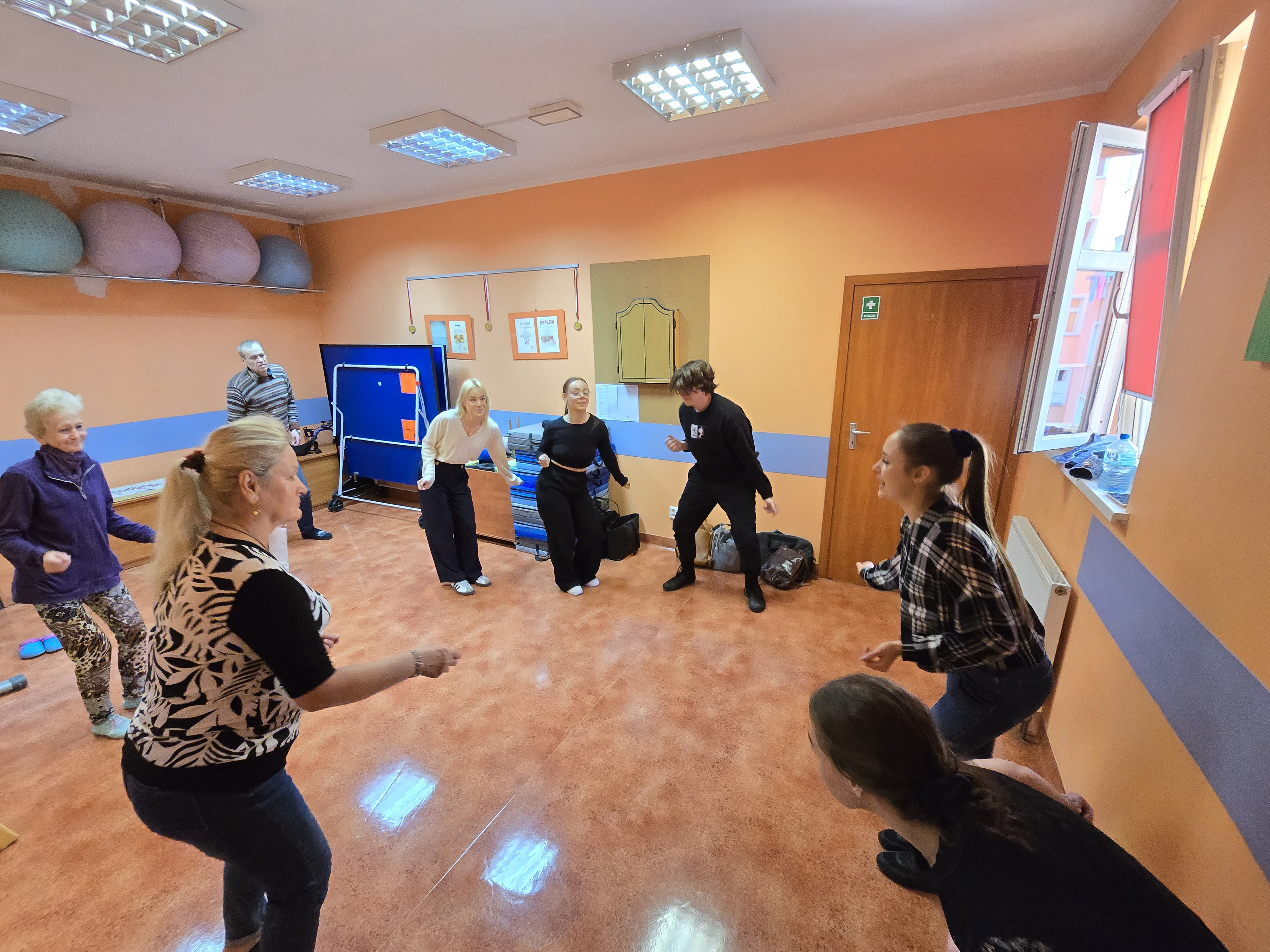 Grupa kobiet i panów wykonuje ćwiczenia taneczne.
