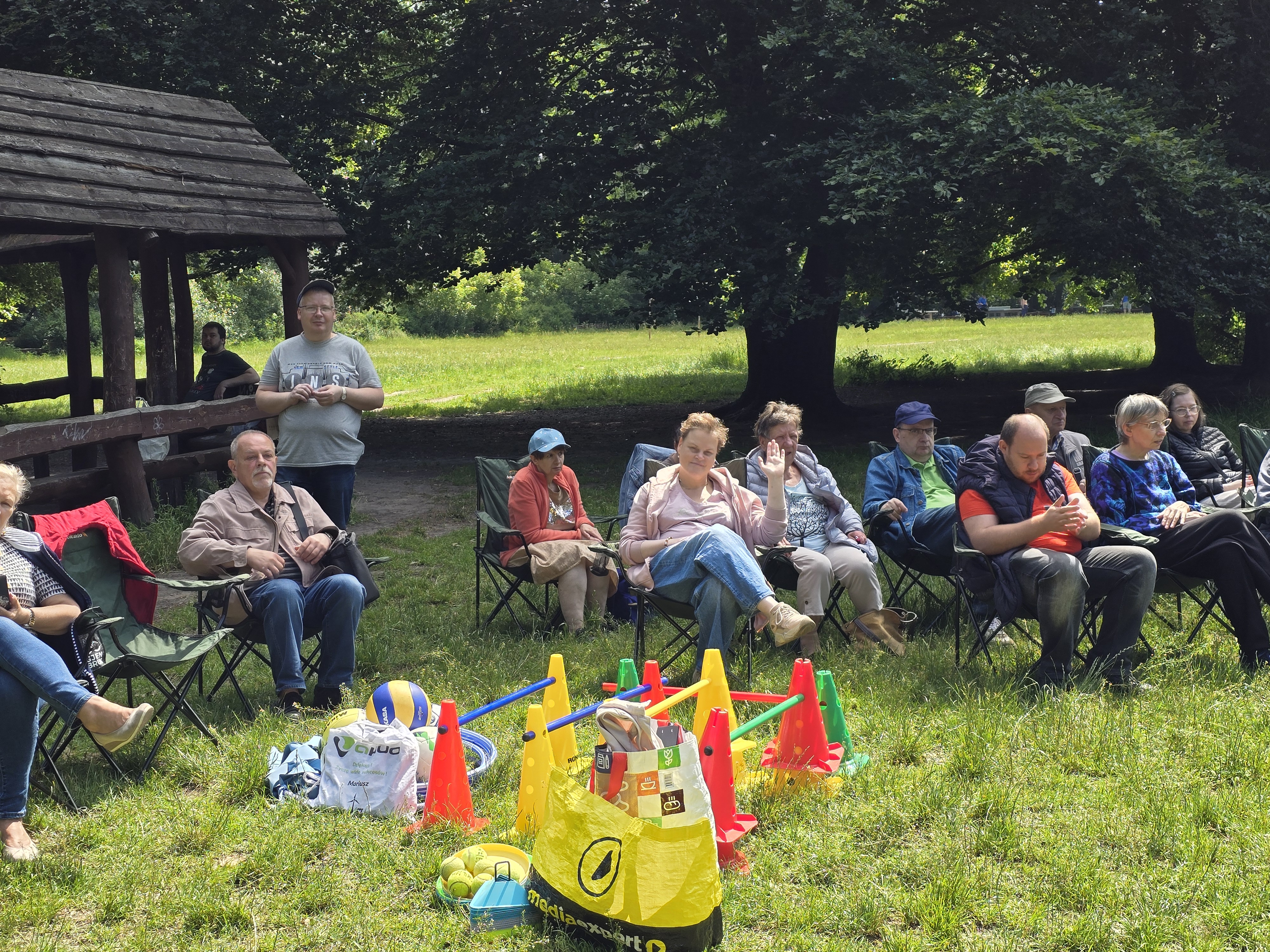 Grupa osób siedzi na fotelach turystycznych na polanie leśnej.