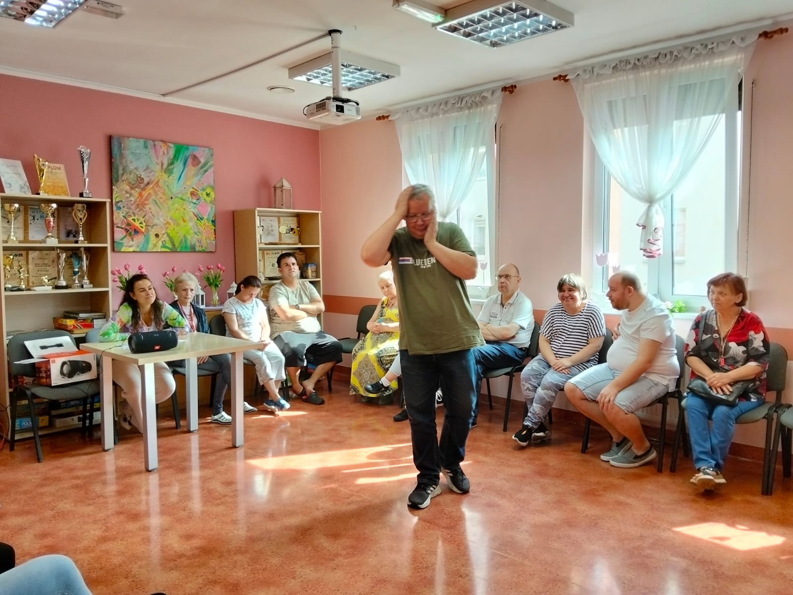 Grupa osób siedzi w kręgu na środku sali mężczyzna cos prezentuje.