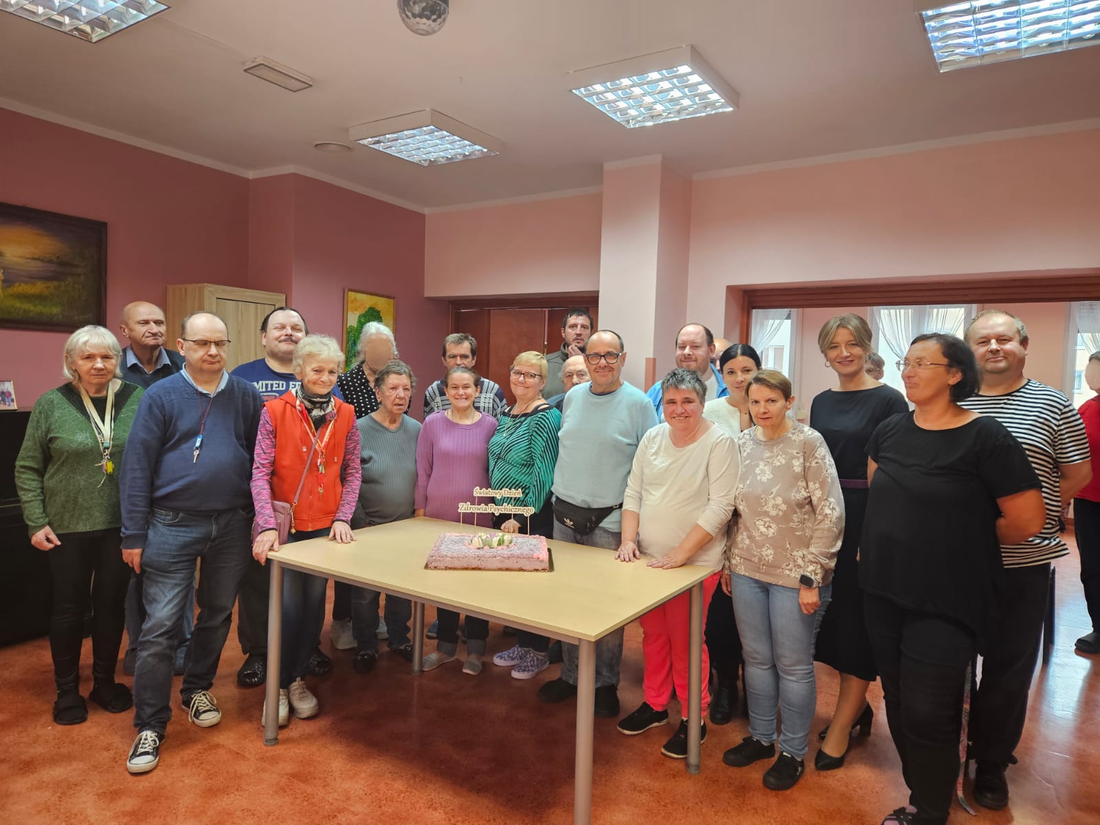 Grupa osób stoi przy stole na którym widnieje tort z okazji Dnia zdrowia psychicznego.