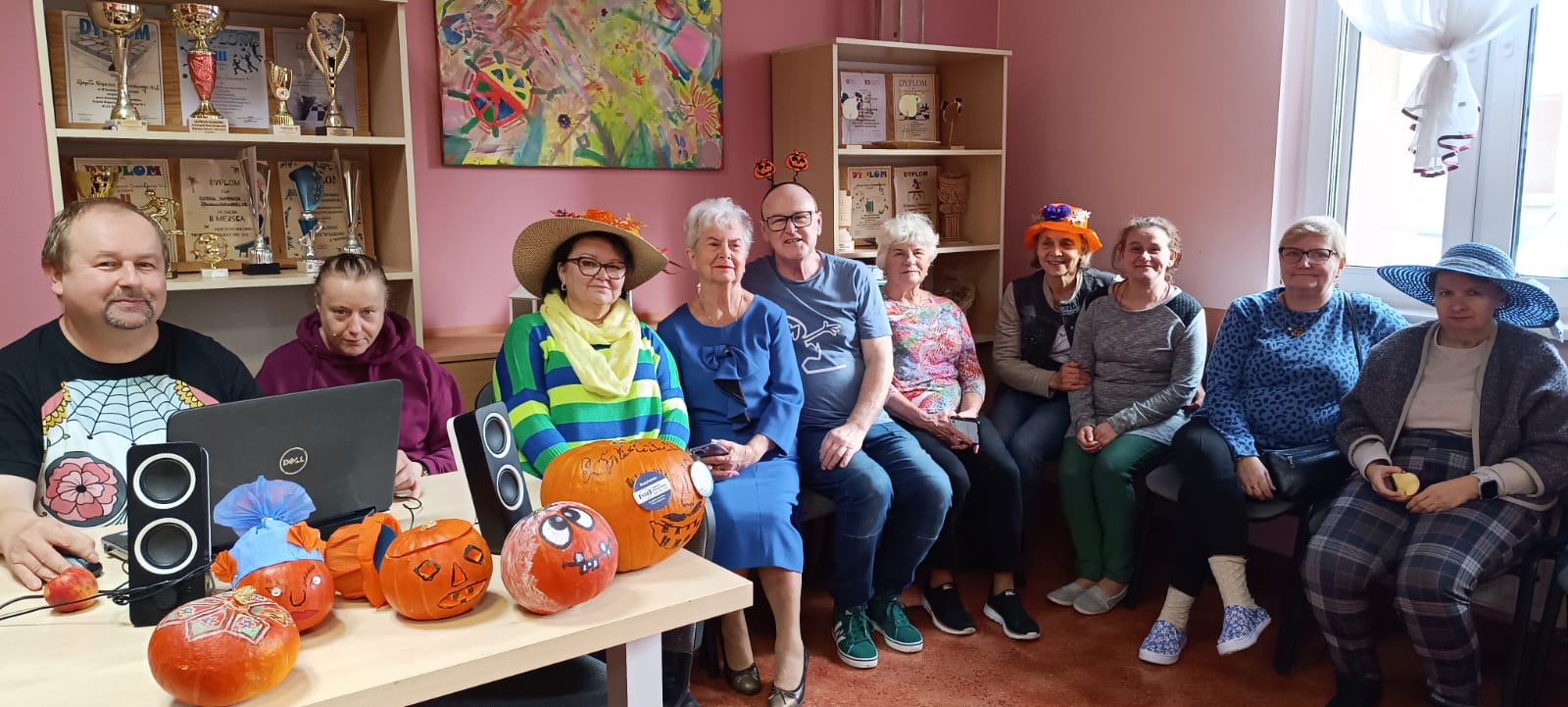 Grupa osób siedzi z dyniami na stole i paterzy w obiektyw.