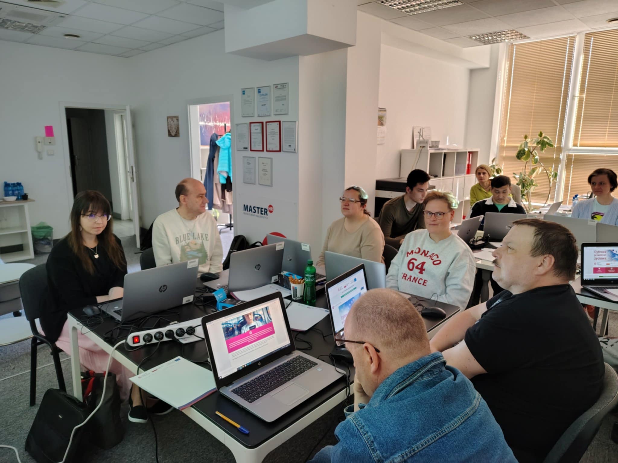 grupa osób siedzi przy monitorach.