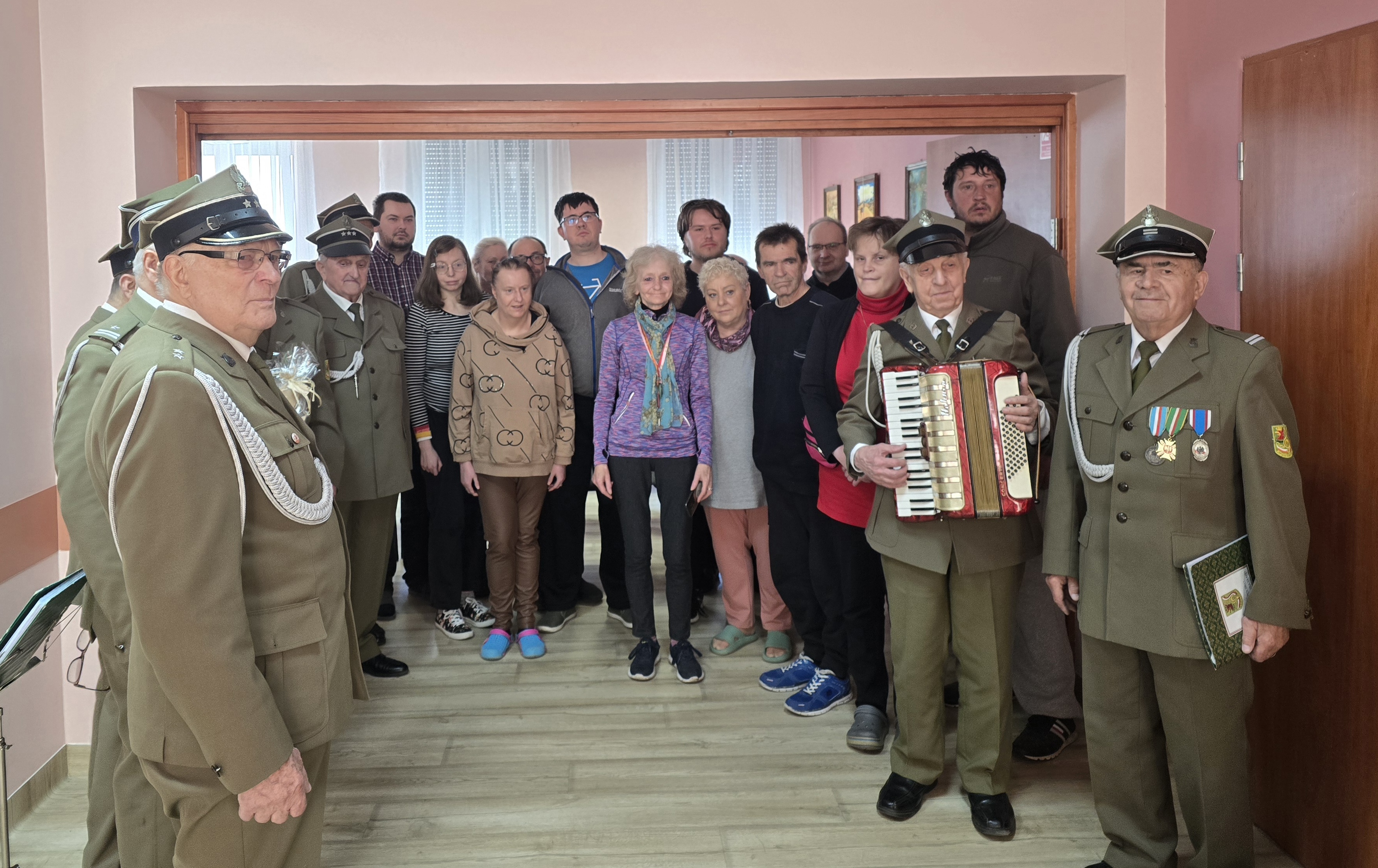 Grupa osób stoi z chórem mężsczyzn w starszym wieku ubranych w mundury wojskowe.