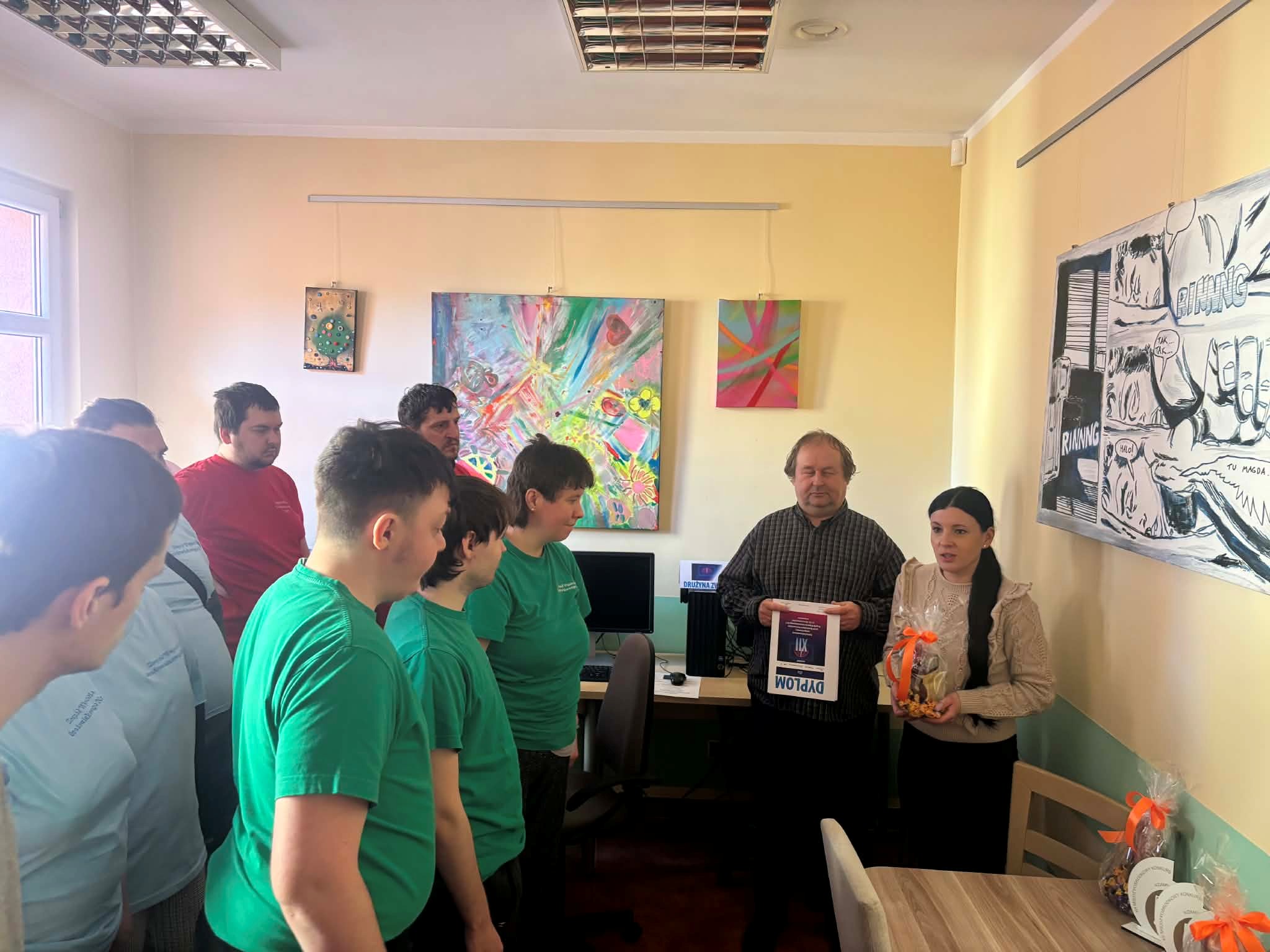 Kobieta z nagrodą i mężczyzna stoją przed grupą osób w pracowni komputerowej.