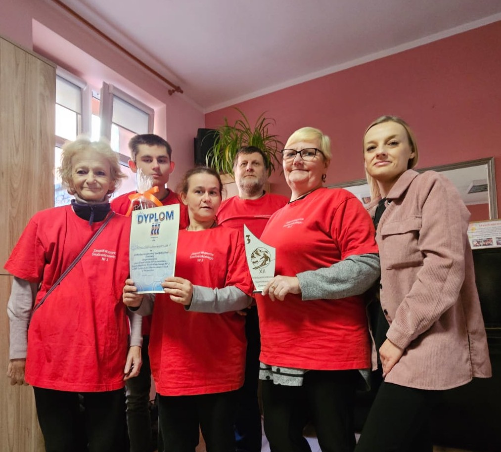 Drużyna w czerwonych koszulkach ,cztery kobiety i dwóch mężczyzn ,osby prezentują dyplom trzeciego miejsca i nagrodę puchar.