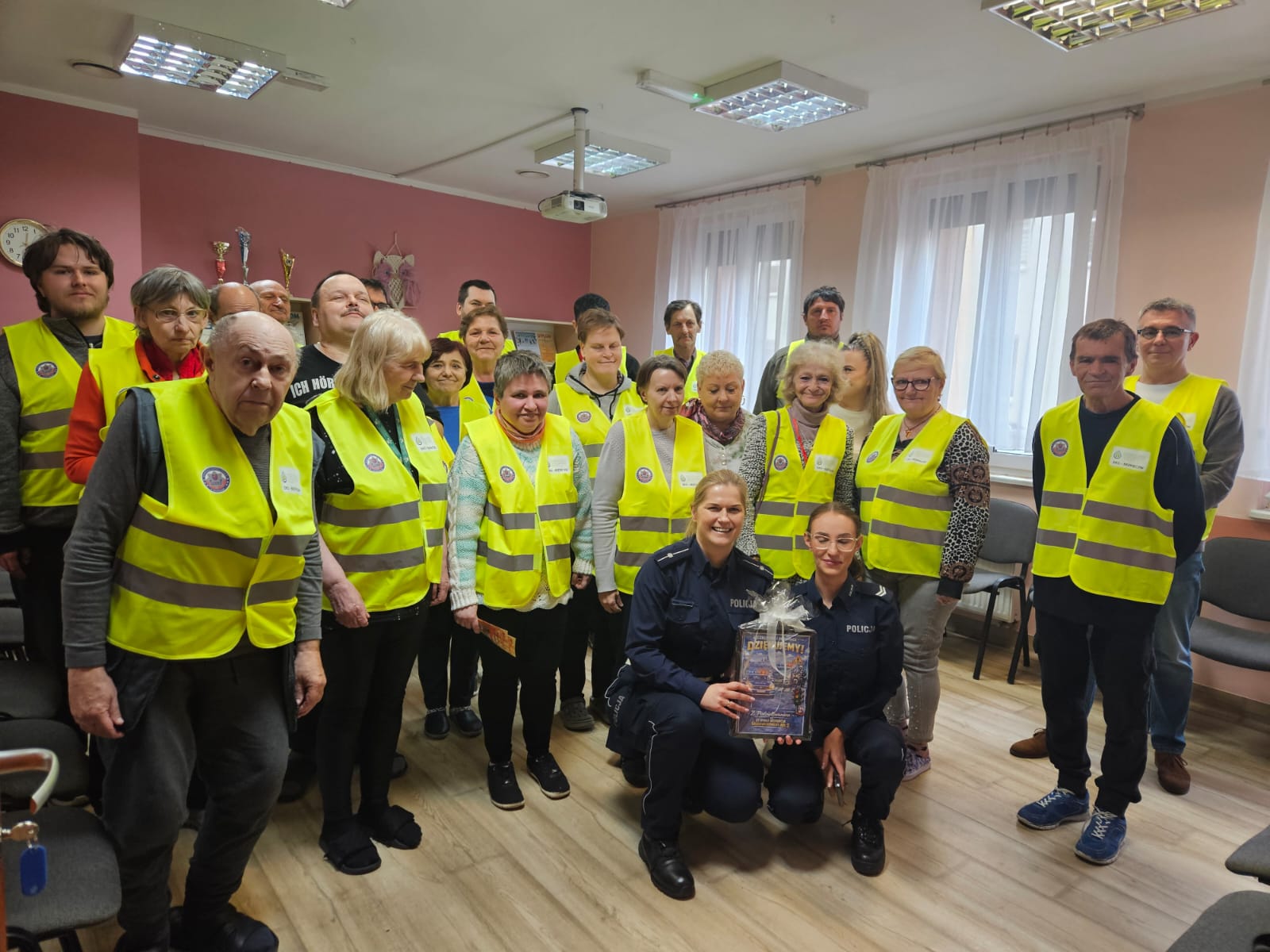 Grupa osób w kamizelkach odblaskowych pozuje do zdjęcia z funkcjonariuszkami policji drogowej.