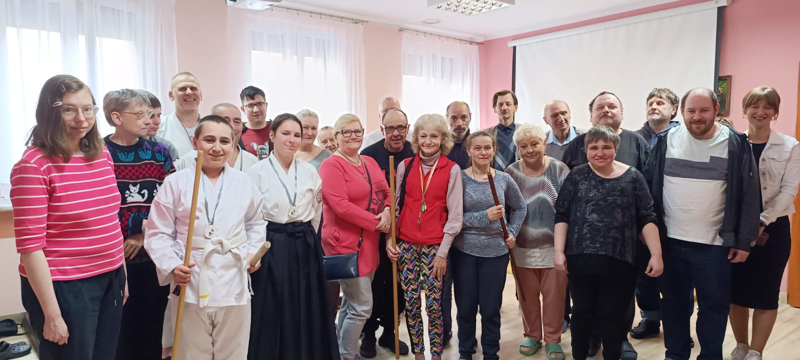 Grupa uczestników stoi na pustej sali z zawodnikami Aikido.