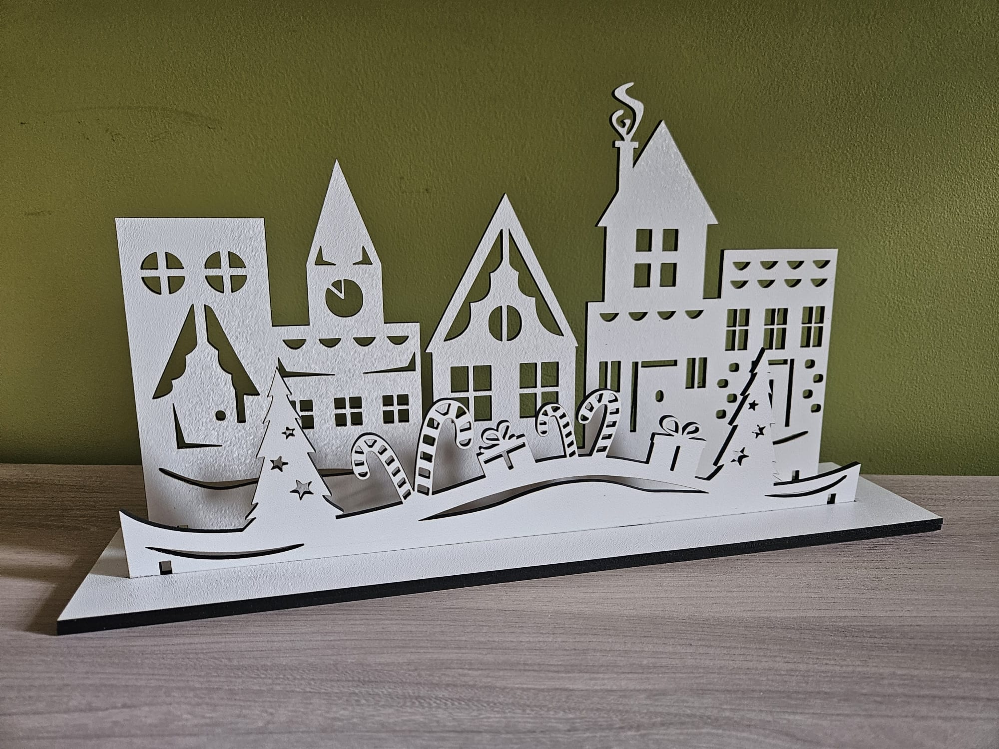 Biała, ażurowa dekoracja przedstawiająca zimowe miasteczko.