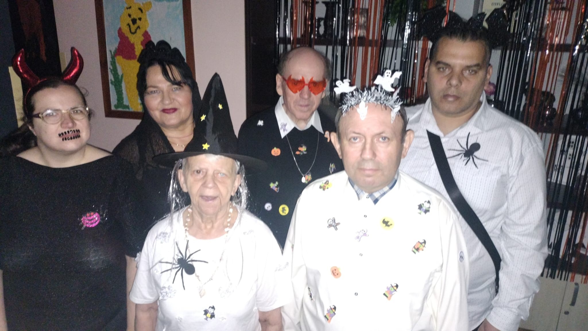 Grupa pięciu osób pozujących do zdjęcia. Osoby są przebrane w kostiumy. W tle widać obraz oraz wiszące dekoracje.