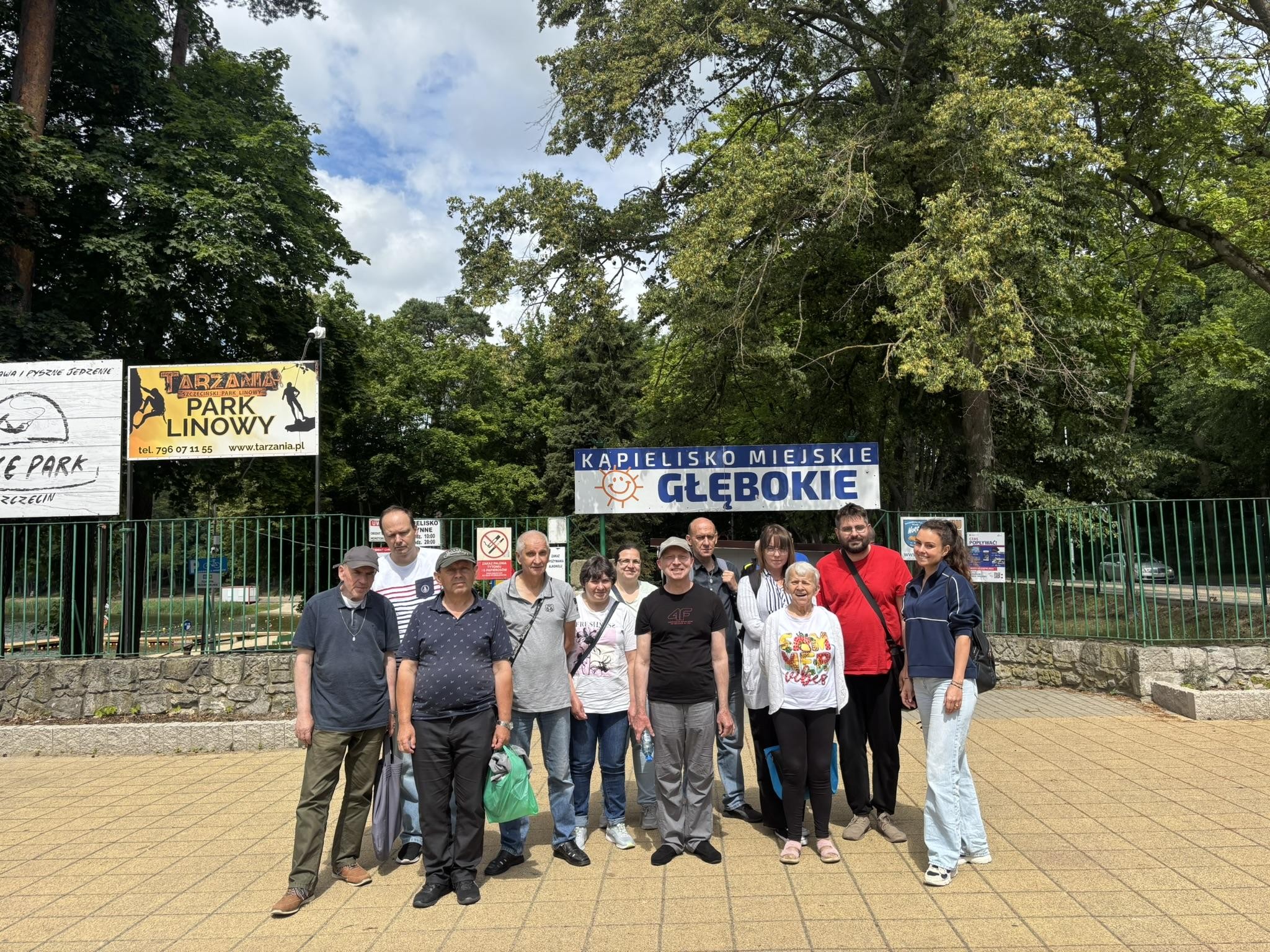 Grupa osób stojąca przed wejściem na kąpielisko miejskie „Głębokie”.