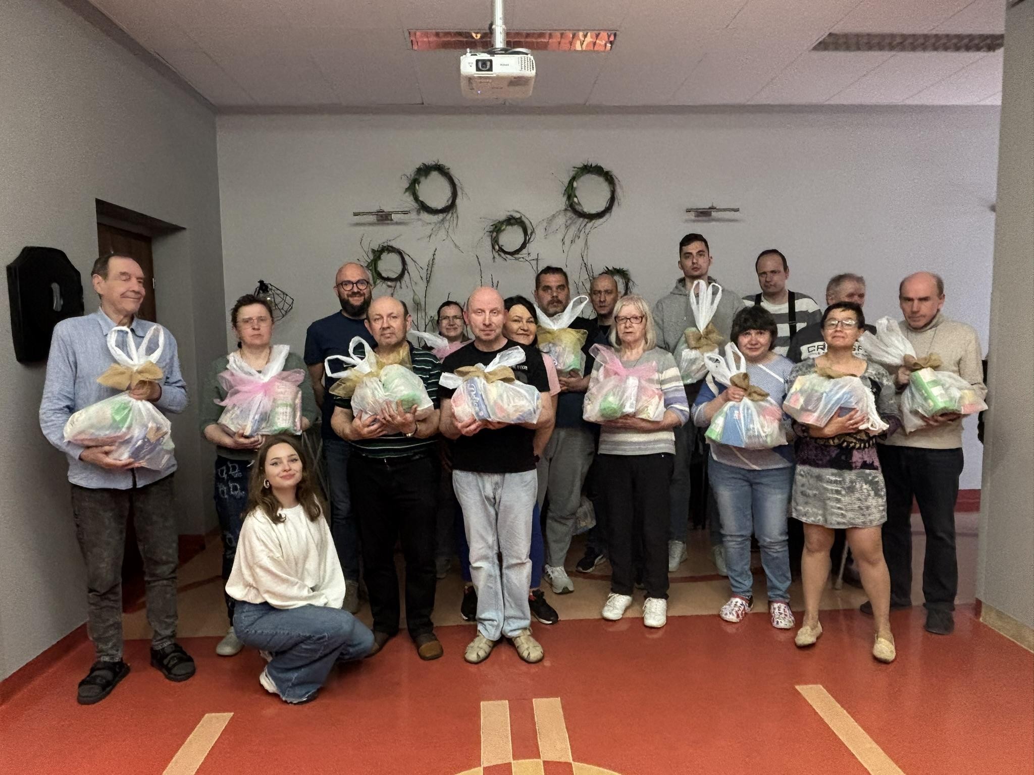 Grupa osób pozująca na tle ściany. Osoby trzymają paczki.