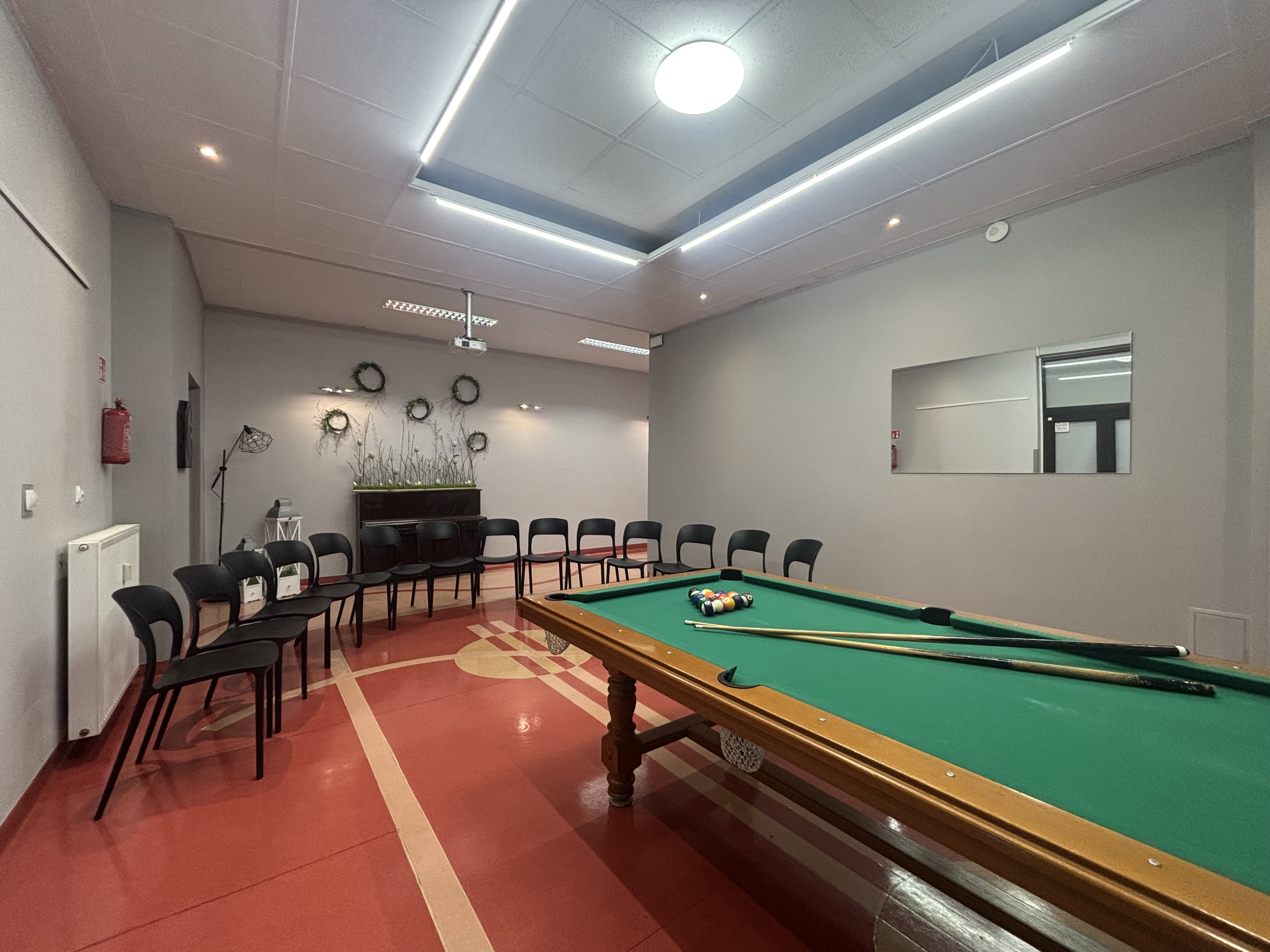 Pomieszczenie bilardowe ze stołem bilrdowym z czarnymi krzesłami.