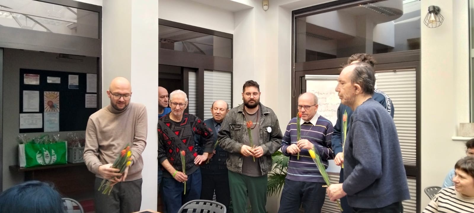 Grupa mężczyzn trzymająca tulipany. W tle widać okna i tablicę.